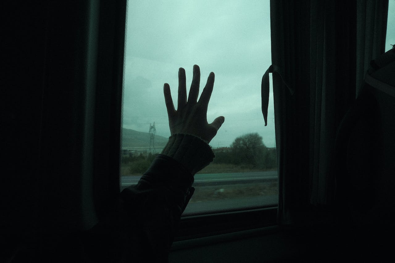 una mano appoggiata su un finestrino da cui si vede un paesaggio naturale arido